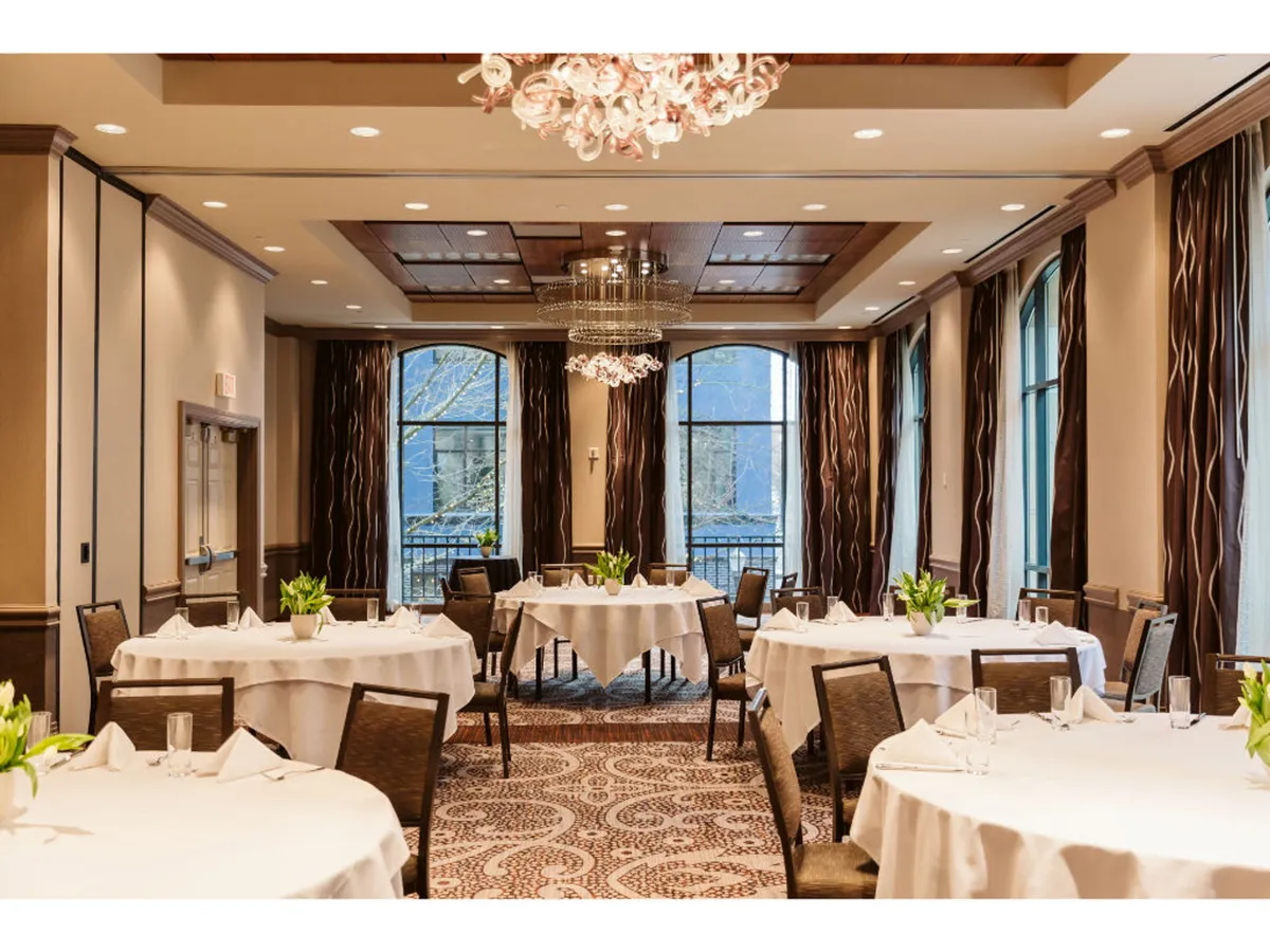 A sophisticated dining area highlighted by a grand chandelier, elegantly decorated tables, and large windows that hint at panoramic views beyond, exuding an atmosphere suited for romantic dinners and special occasions.