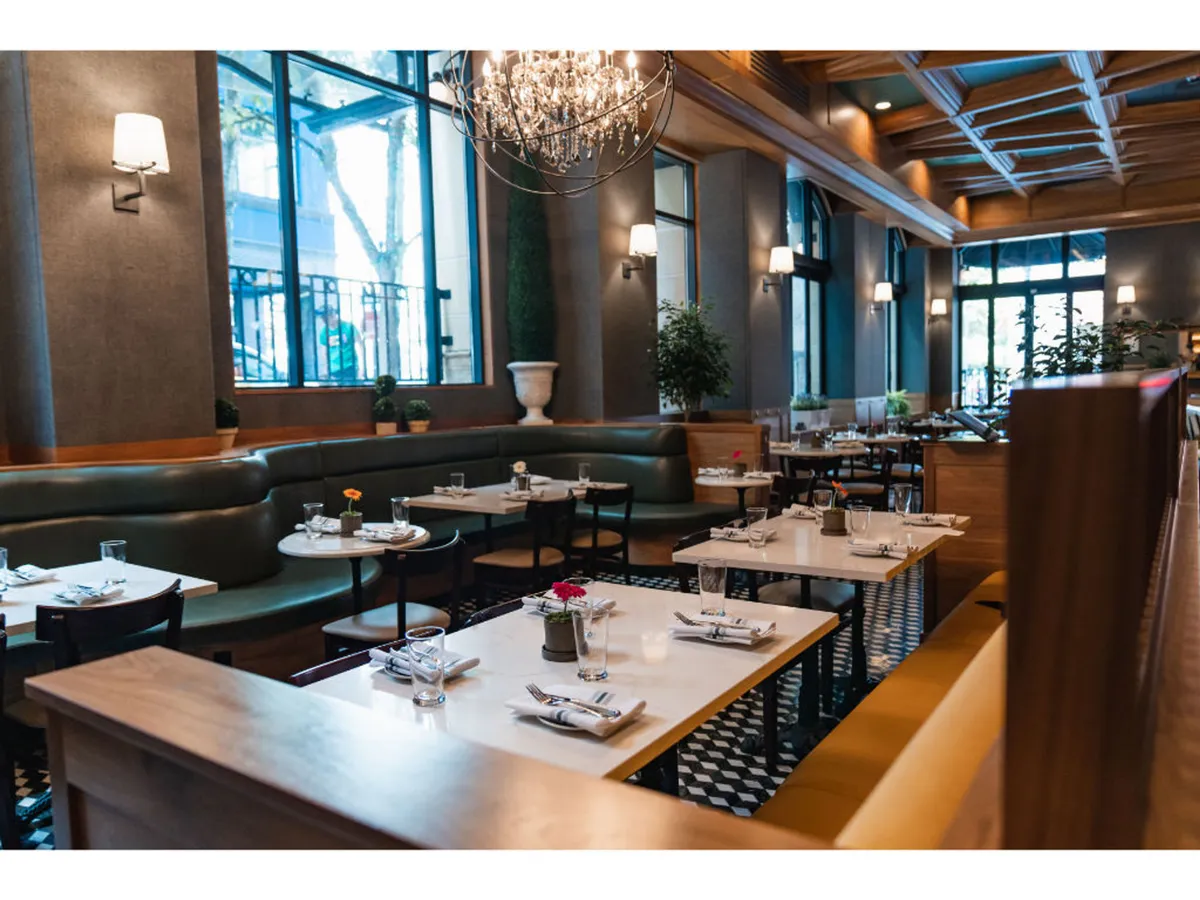 A stylish dining and lounge space with a grand chandelier, plush green seating, decorative plants, and large windows. The setting is sophisticated yet comfortable, ideal for informal meetings or unwinding with colleagues.