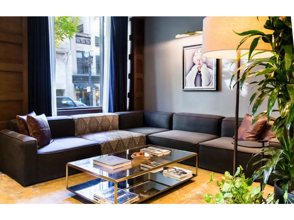 A modern, comfortable lounge area with a large sectional sofa, artful wall decor, a coffee table with books, and lush green accents. The space is filled with soft, natural light and encourages relaxation, socializing, and a sense of home-like comfort.