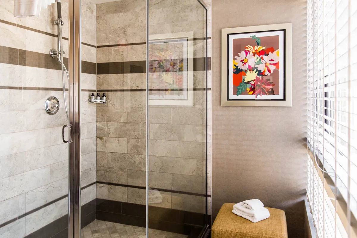 A vibrant and modern bathroom with a glass shower enclosure, colorful artwork on the wall, and neatly arranged towels. Natural light filters into the space, emphasizing its refreshing and inviting ambiance.