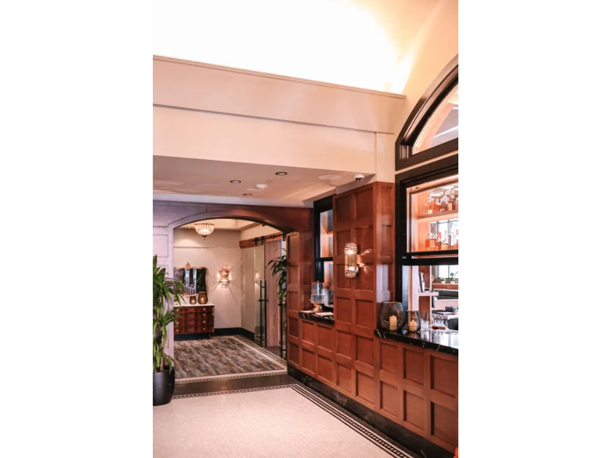 The image highlights a refined reception area with rich wood paneling, an elegant chandelier, a well-appointed desk, and a vibrant green plant. The setting suggests both first impressions and an area where guests interact with attentive staff for any need.