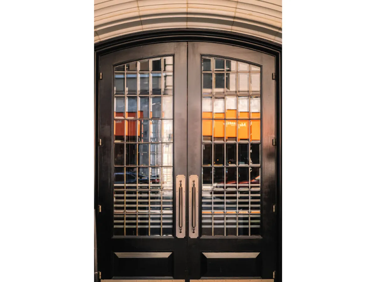 A striking exterior shot showcasing ornate double doors with decorative glass panels and stylish door handles. Warm lighting spills from within, inviting guests into an elegant, urban setting that hints at the excitement and sophistication inside.